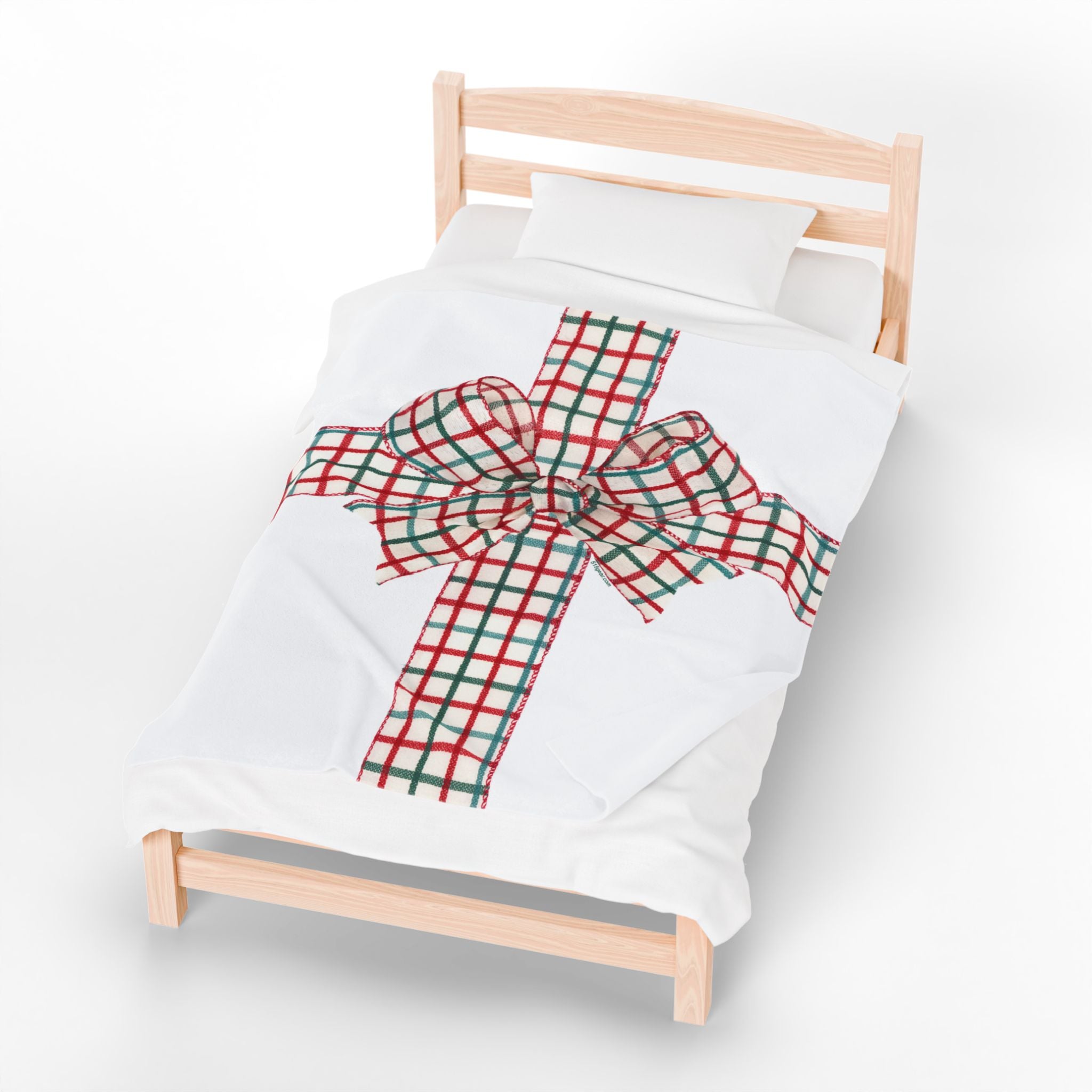 White blanket with a red and green plaid holiday bow graphic on a wooden bed frame against a white background