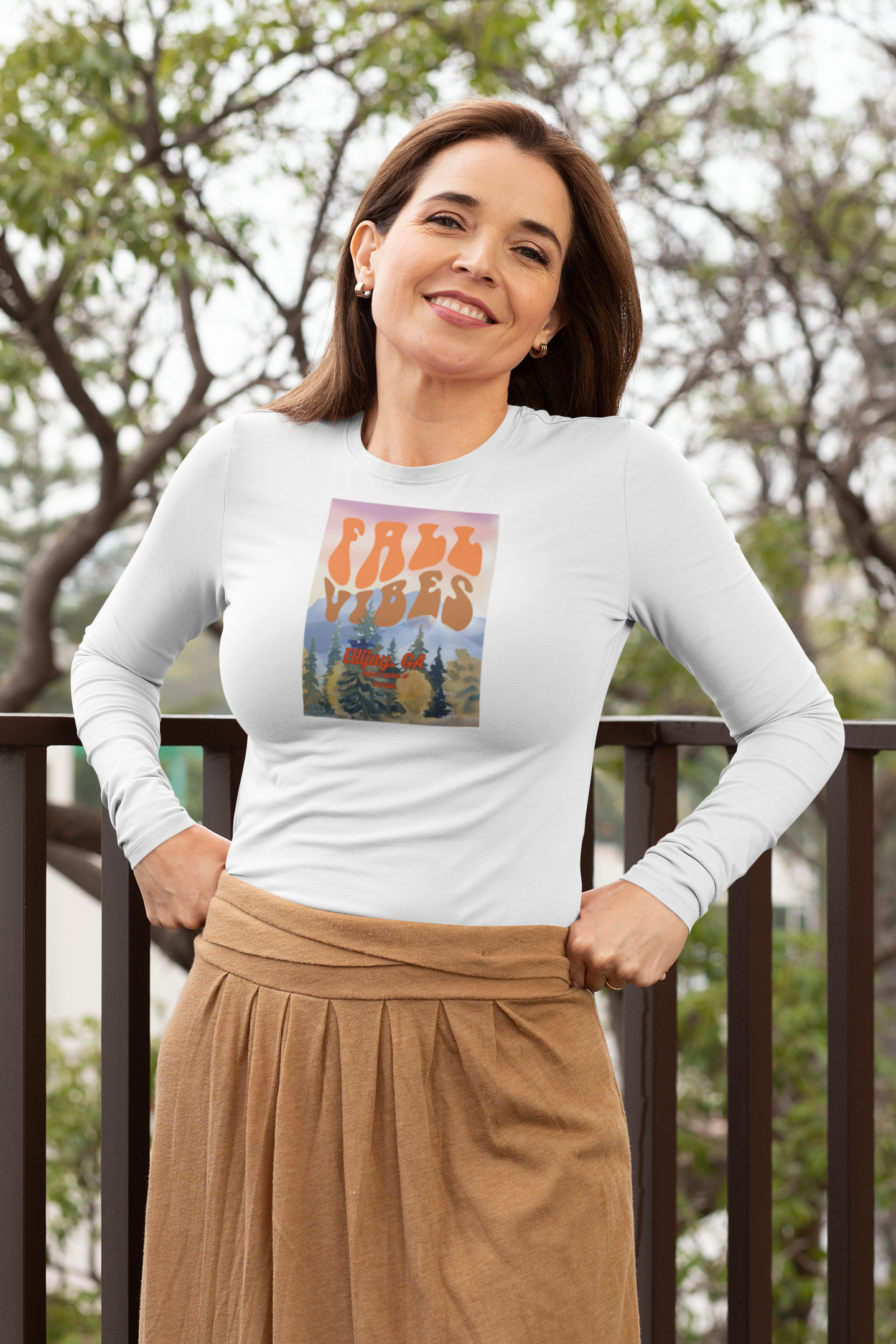 Woman wearing a white long-sleeve unisex tee with a outdoor graphic of trees and mountain and text "Fall Vibes Ellijay GA - Apple Capital of Georgia"