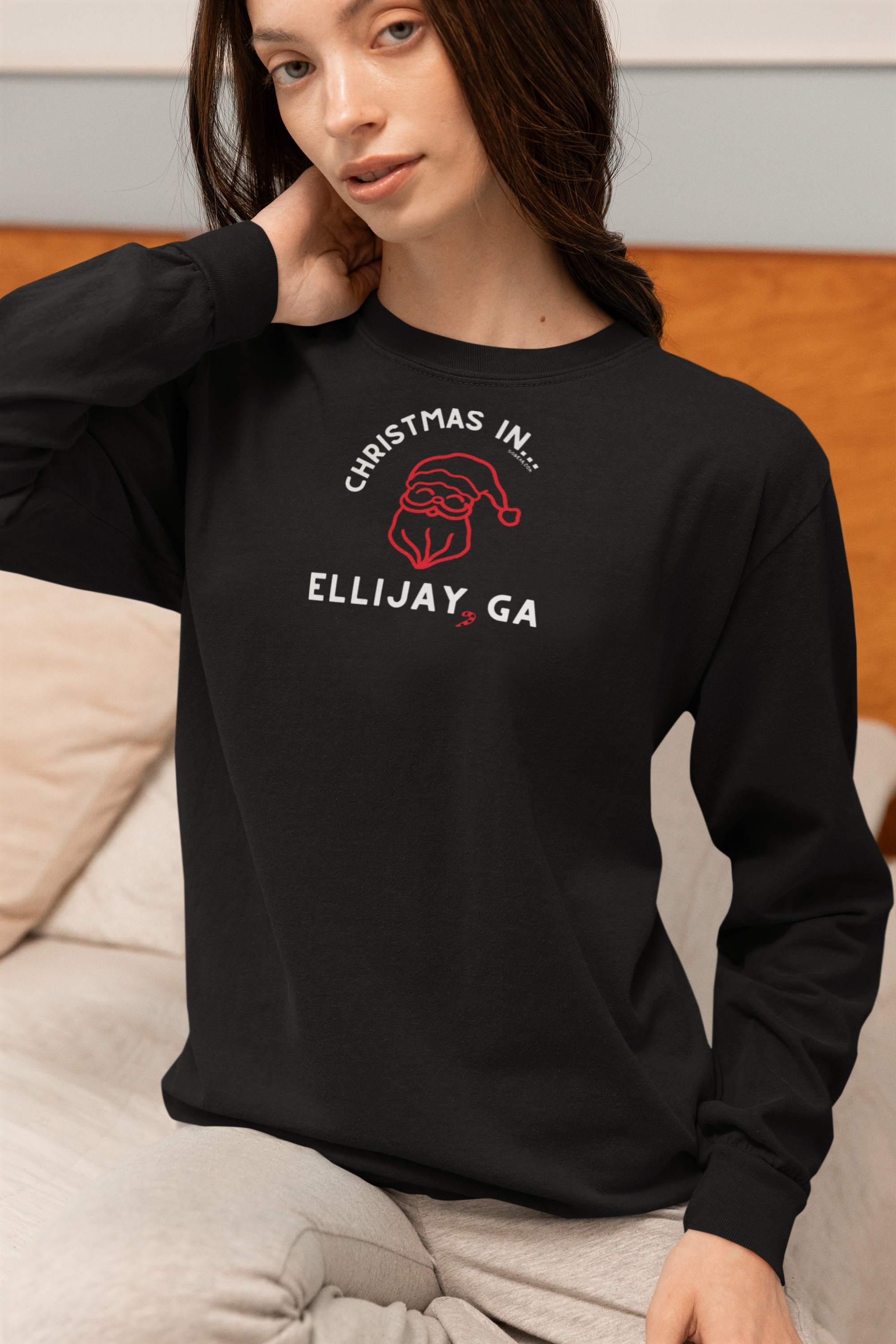 Woman wearing a black long sleeve comfort comfort t-shirt with 'Christmas in Ellijay, GA' text and Santa Claus graphic.