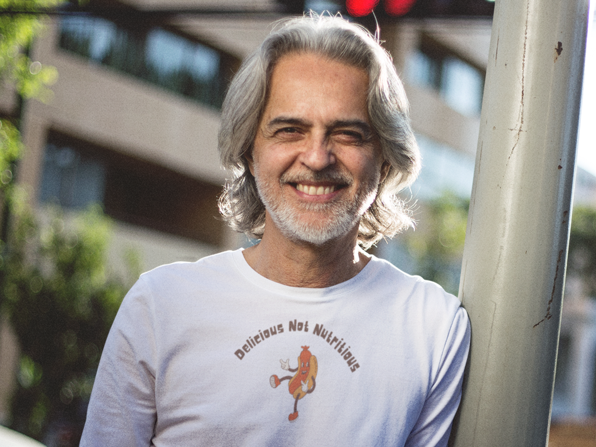 Man wearing a white long sleeve t-shirt with hotdog graphic and text "Delicious Not Nutritious"