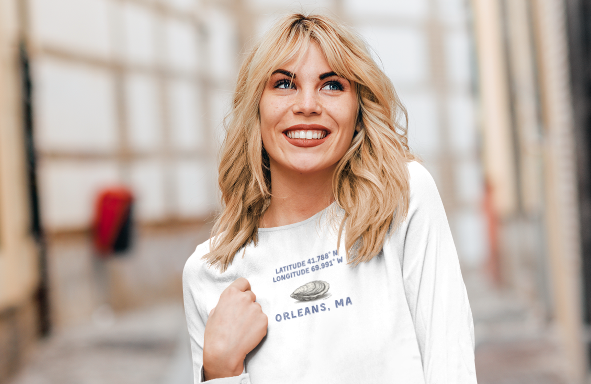 Woman wearing a white long-sleeve T-shirt with Oyster graphic and text "Latitude 41.788 N, Longitude 69.991 Orleans, MA"