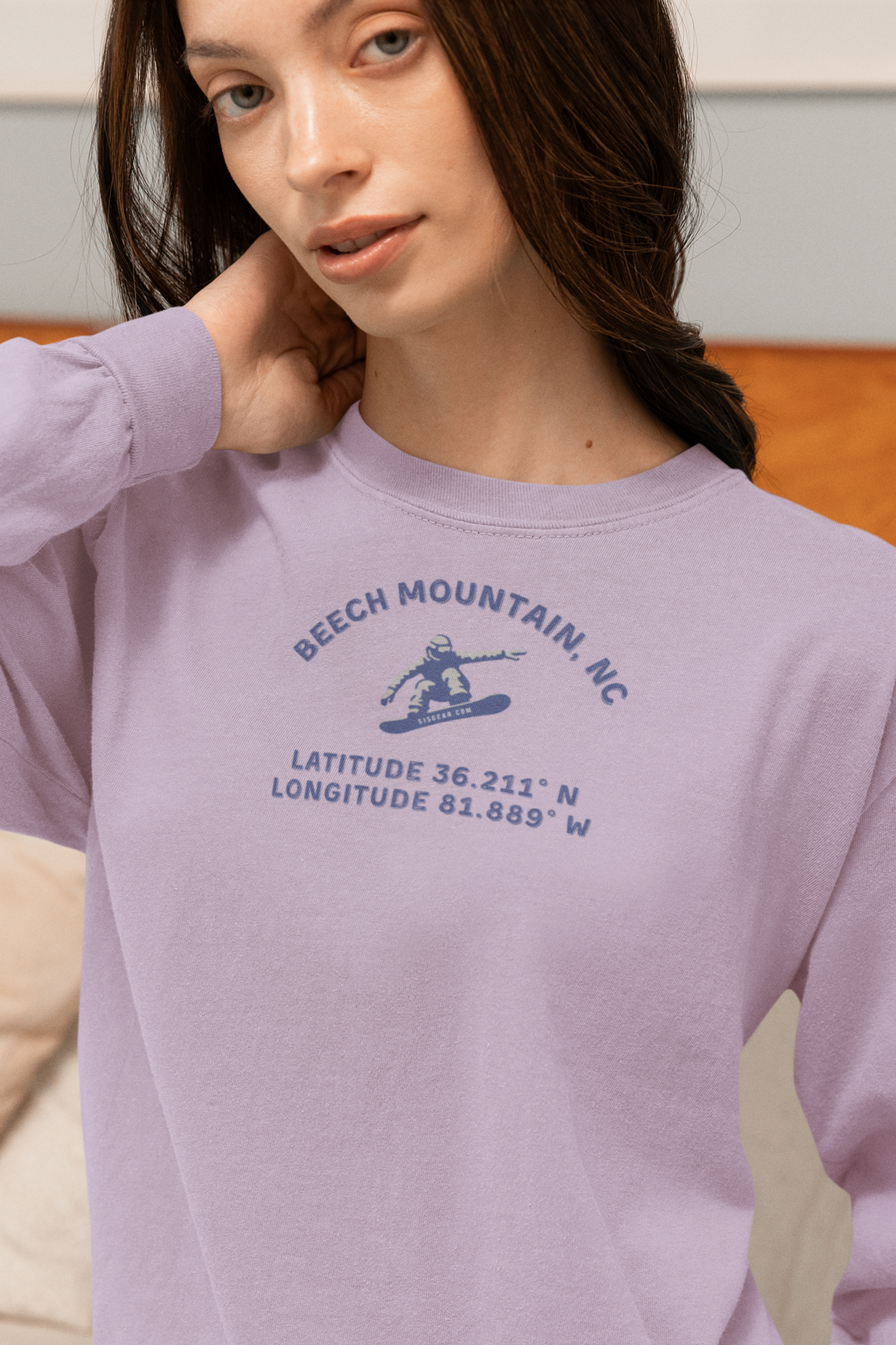 Woman wearing a lavender long sleeve tee with Snowboarder mid-air and text 'Beech Mountain, NC Latitude 36.211' N Longitude 81.889' W