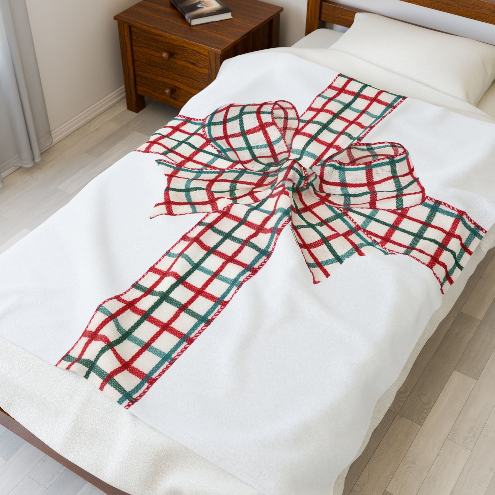 White blanket with a red and green plaid holiday bow graphic on a bed in a bedroom setting.