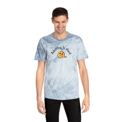 Person wearing a light blue tie-dye Comfort Colors 1745 unisex color blast t-shirt, 100% ring-spun cotton, with melting smiley face and text "Adulting is Hard"