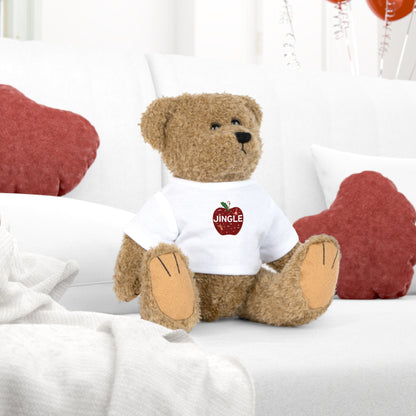 Teddy bear wearing a white shirt with a red apple graphic and 'JINGLE' text, sitting on a white surface 