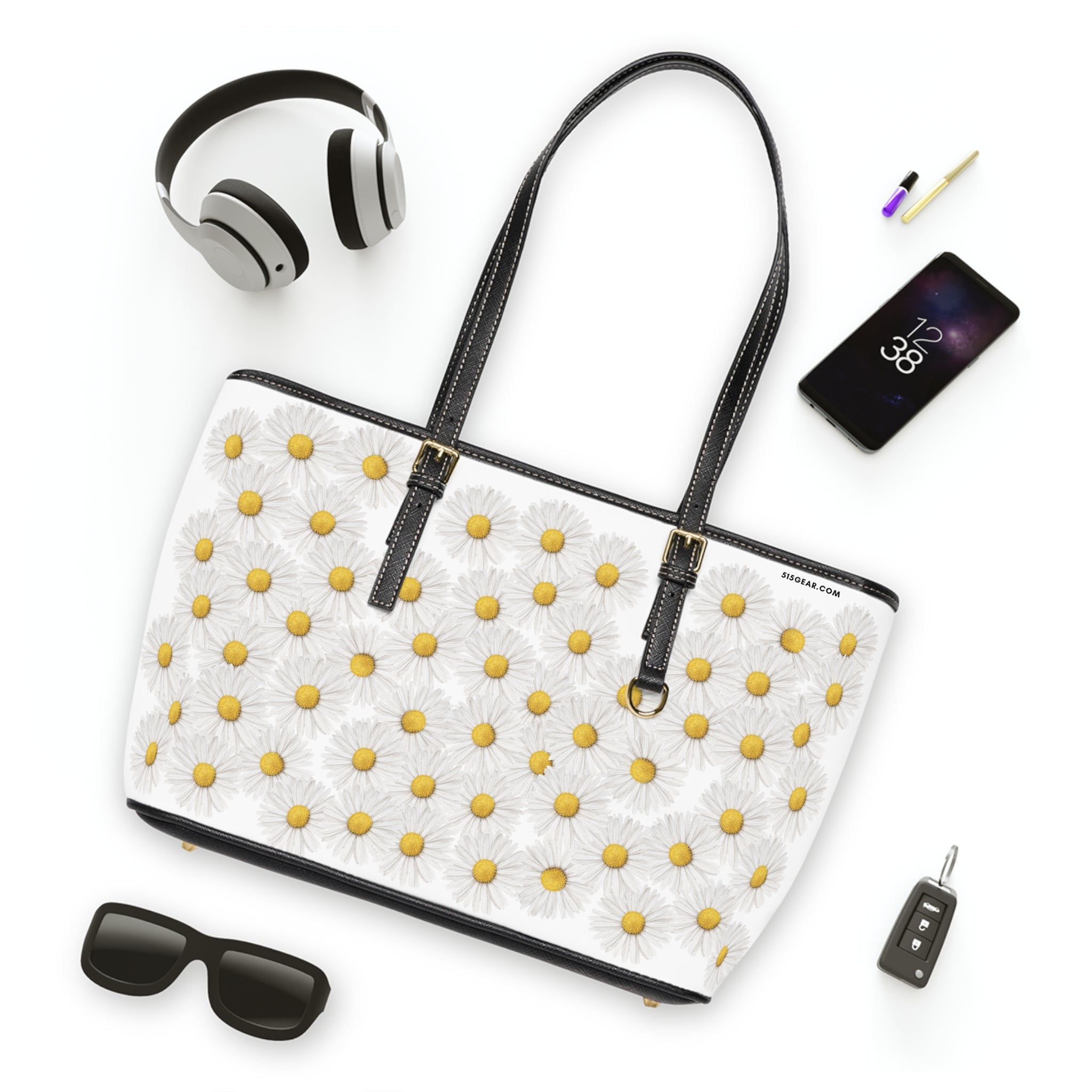 White tote bag with yellow floral daisy pattern, surrounded by black headphones, phone, sunglasses, and car key on a white background.