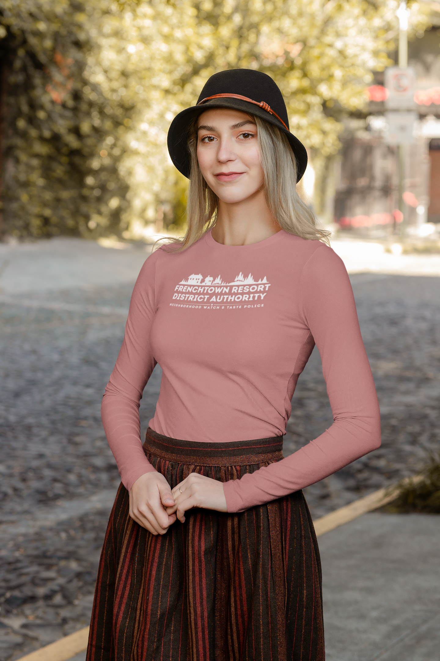 Woman wearing a Blush Rose long-sleeve tee with text Frenchtown Resort District Authority Neighborhood Watch & Taste Police