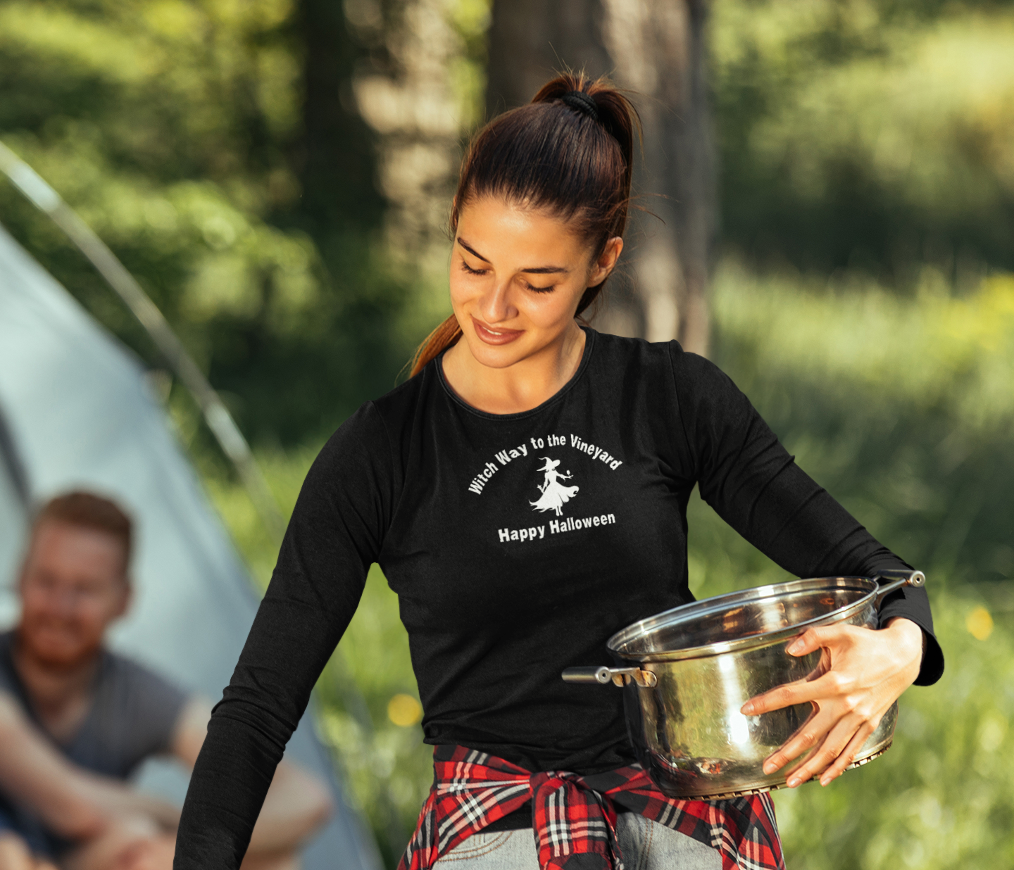 Woman grilling outdoors with a black long-sleeve unisex comfort color t-shirt with halloween witch graphic holding a wine glass  and text "Witch Way to the Vineyard - Happy Halloween" 