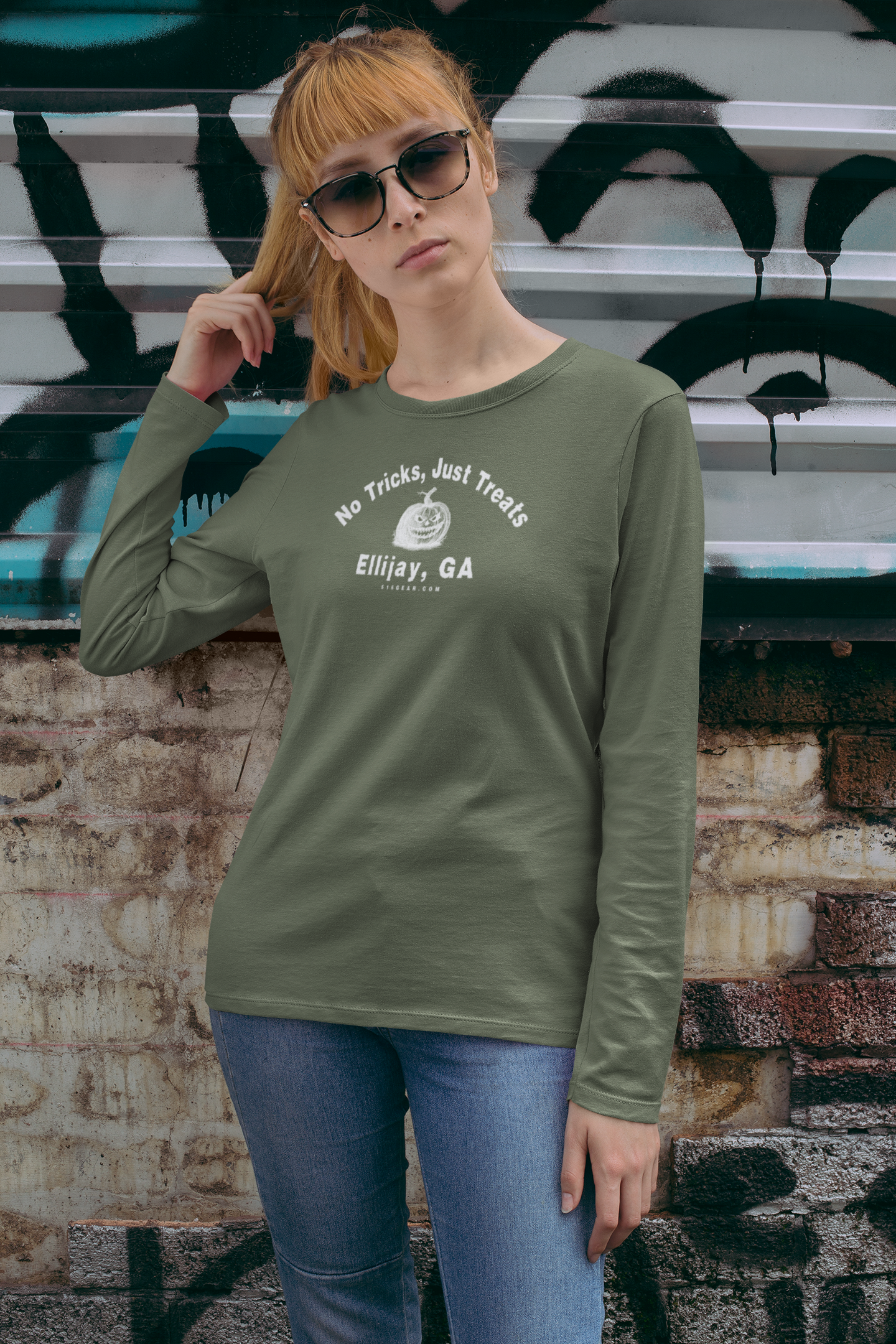 Woman wearing a green unisex long sleeve T-shirt with jack-o-lantern graphic and text "No Tricks Just Treats - Ellijay GA" by 515Gear.com