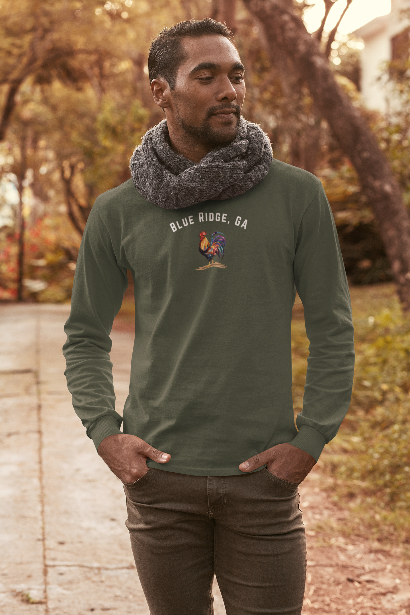 Man wearing a green heather long-sleeve shirt with colorful rooster graphic design and text "Blue Ridge, GA" standing outdoors.