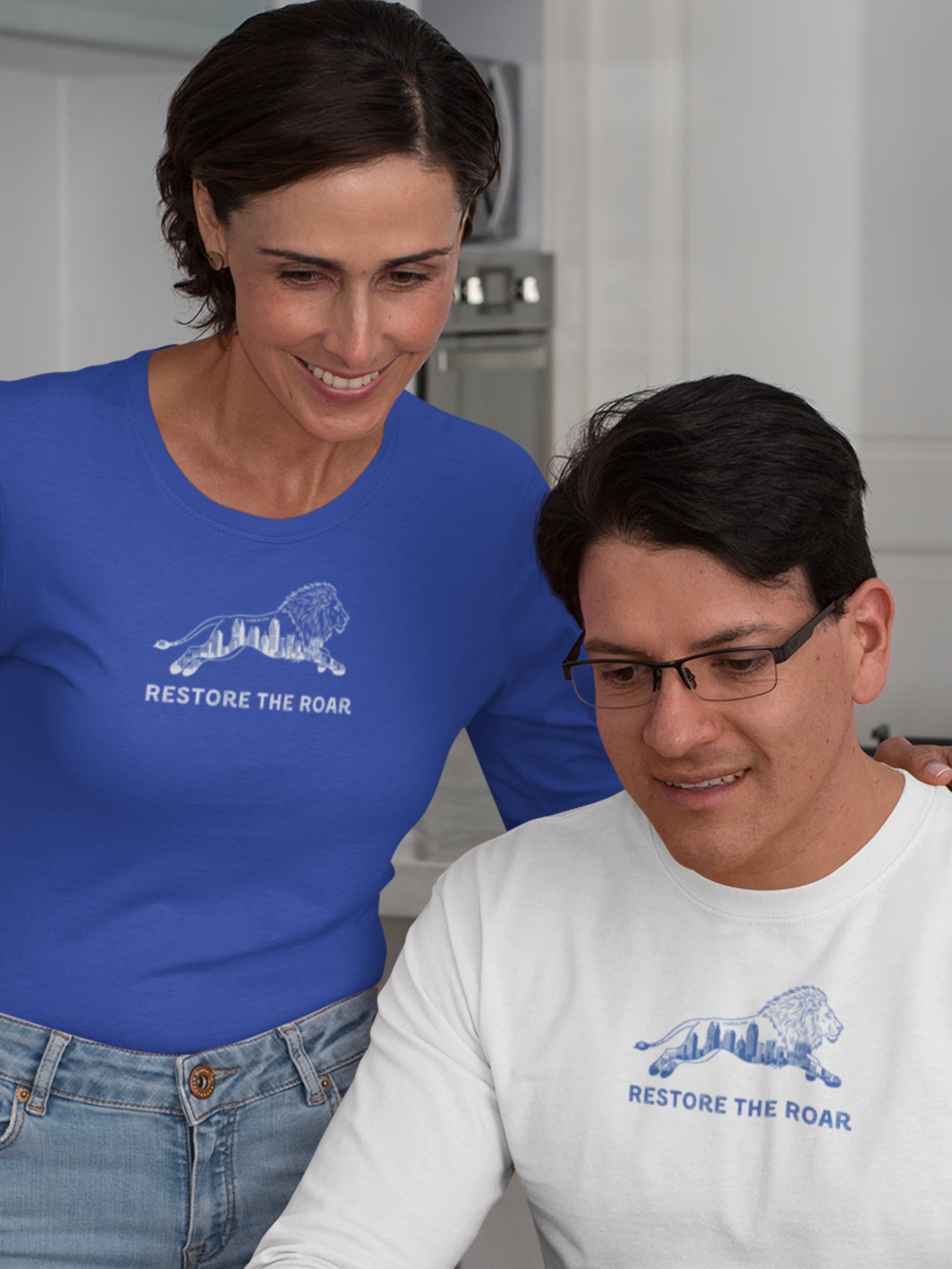 Two people wearing 'Restore the Roar' shirts in a kitchen setting.