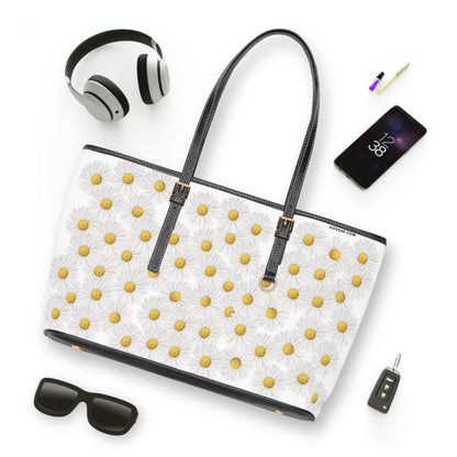 White tote bag with yellow floral daisy patterns, surrounded by accessories on a white background