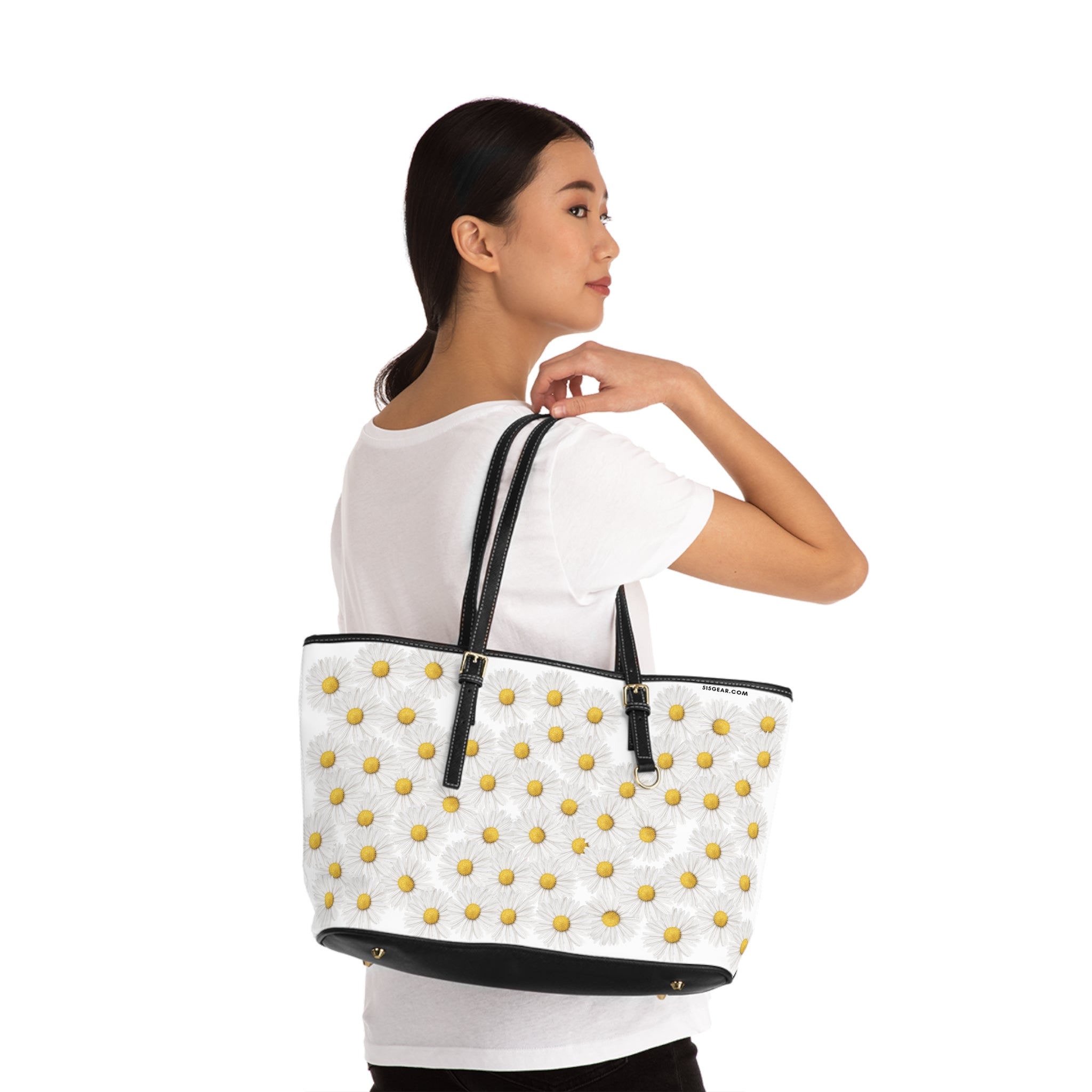 Woman holding a white tote bag with black straps and yellow daisies graphic on a white background